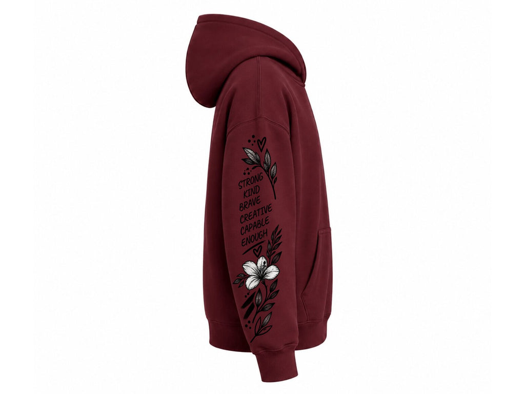 A maroon pullover hoodie shown from the side profile on a plain white background, featuring a black floral graphic and the text 'STRIKE HARD BRING BLOOMS BRING CREATIVE ENOUGH' printed on the sleeve.