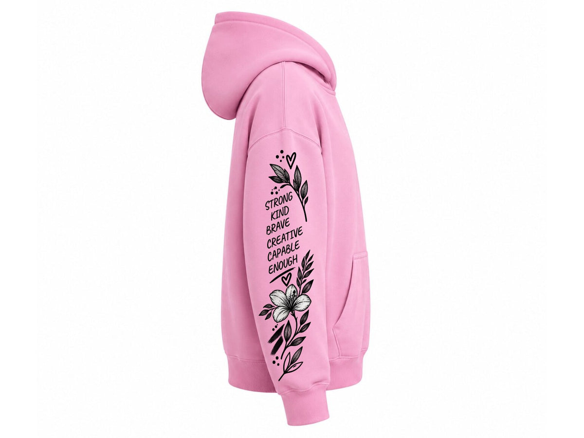 A pink pullover hoodie shown from the side profile on a plain white background, featuring a black graphic print with text and floral illustrations on the left sleeve.