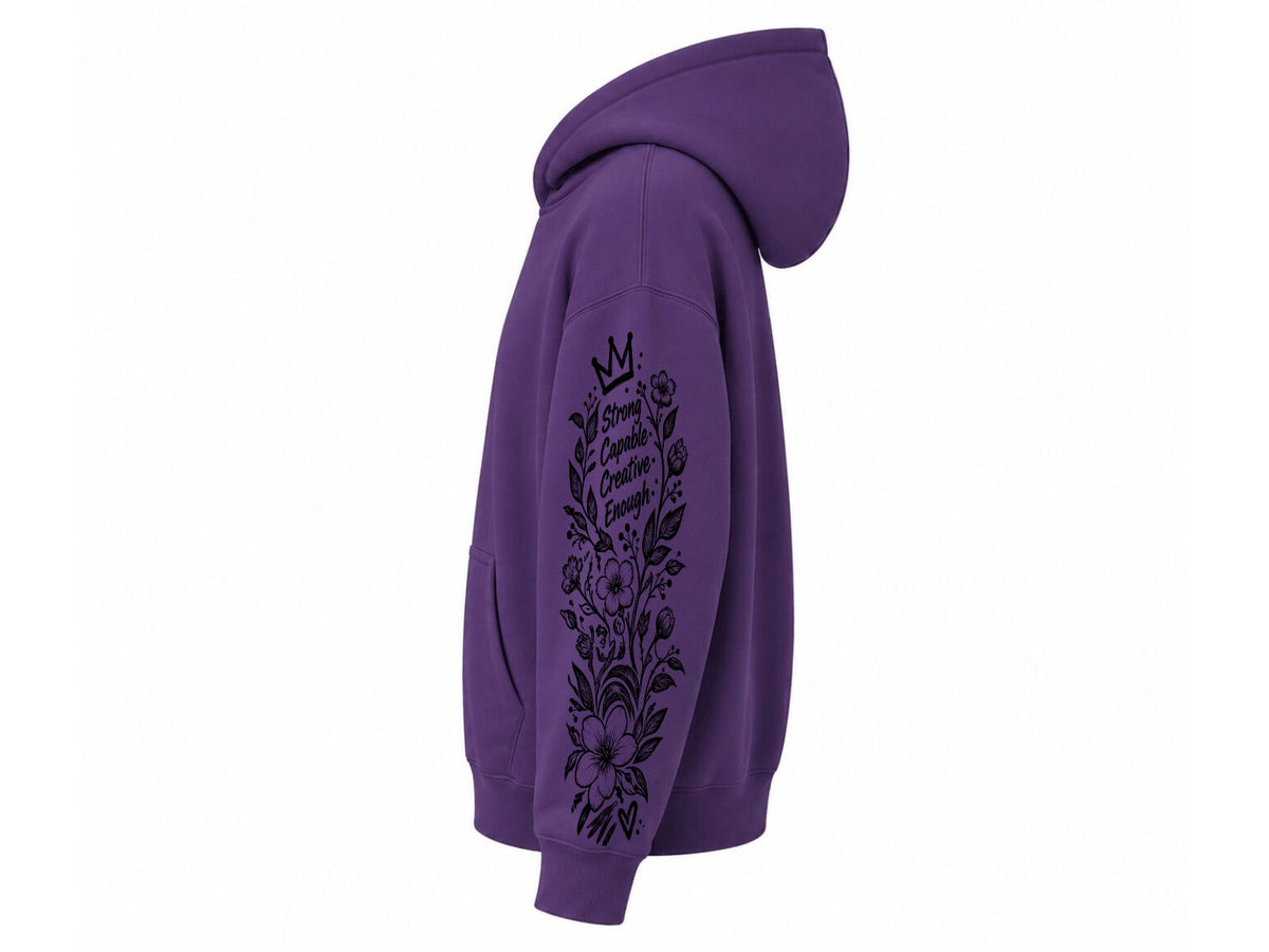 A purple pullover hoodie shown from the side profile, featuring a black floral and crown graphic printed down the right sleeve with the text 'She Who Cares Grows Strong'.